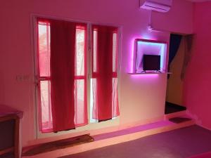 a room with a window with red curtains and a tv at La Maison Blanche in Ndangane