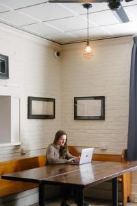 a woman sitting at a table with a laptop at Saintlo Ottawa Jail Hostel in Ottawa