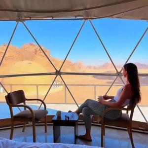 Sultan Luxury Camp في وادي رم: امرأة تجلس على كرسي أمام النافذة