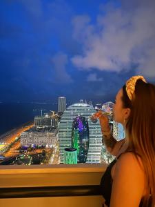 a woman taking a picture of a city at night at Panorama Sea Side Central Batumi in Batumi