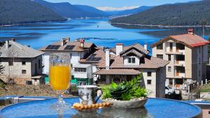 een glas sinaasappelsap op een tafel met uitzicht op een meer bij ЕЛЕГАНС къща за гости in Dospat