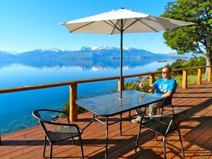 a man sitting on a deck with a table and an umbrella at Terra Luna Lodge in Puerto Guadal