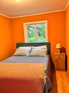 a bedroom with orange walls and a bed with a window at the house of flowers in Osorno