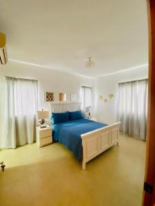 biała sypialnia z niebieskim łóżkiem i białymi zasłonami w obiekcie Beach/ Pool Apartment Cadaques Bayahibe w mieście La Romana