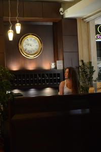 a woman sitting in front of a clock on a wall at Central Hotel in Paralia Katerinis