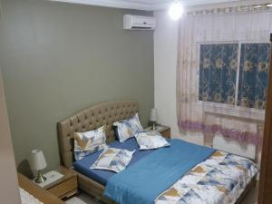 Schlafzimmer mit einem Bett mit blauer Bettwäsche und einem Fenster in der Unterkunft Panorama III Cliniques les Jasmins in Ariana
