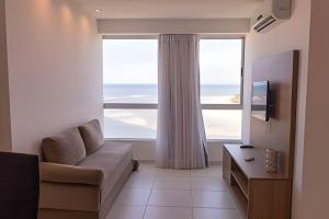 a living room with a couch and a large window at Hosts BR - Flats Frente Mar c/ Cozinha in Recife