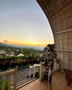 a woman standing on a balcony looking out at the sunset at The Blooms Villas in Bedugul