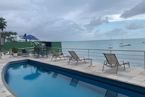 einen Pool mit Stühlen, einem Tisch und dem Meer in der Unterkunft Hosts BR - Cobertura duplex frente mar in Fortaleza