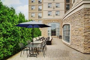 un patio con mesas, sillas y sombrilla en Staybridge Suites Oakville Burlington, an IHG Hotel, en Oakville