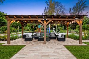a pergola with couches and chairs on a patio at Luxurious 8BR Dream Estate w Private Heated Pool in Pompano Beach