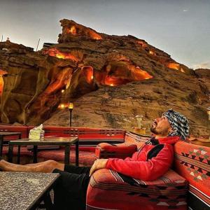 a man sitting in a chair in front of a rock wall at WADI RUM STAR WARS CAMP in Wadi Rum