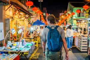 a man with a backpack walking through a market at Homestay 3 rooms suite Apartment 8-10pax at Amari Villa Bukit Katil, Ayer Keroh Melaka in Melaka