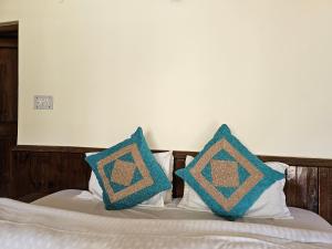 a bed with two blue pillows on it at Purnima Guest House in Manāli
