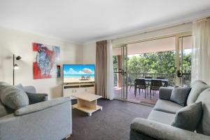 ein Wohnzimmer mit einem Sofa, einem TV und einem Tisch in der Unterkunft Terralong Terrace Apartments in Kiama