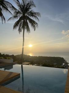 a palm tree sitting next to a swimming pool with the sunset at Blue Bay Villa in Haad Yao