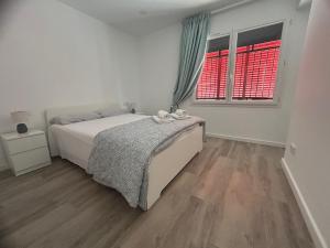 a white bedroom with a bed and two windows at Canyelles BBQ Apartment in Lloret de Mar