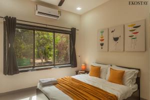 ein Schlafzimmer mit einem Bett mit orangefarbenen Kissen und einem Fenster in der Unterkunft EKOSTAY - Forestwood Villa in Alibag