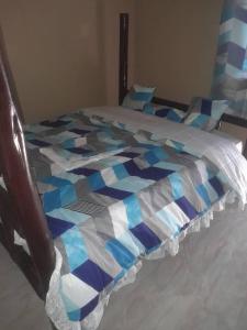 a bed with a blue and white quilt on it at KWERI GUEST HOUSE in Mbarara