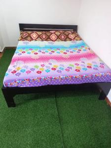 a bed with a colorful comforter on top of green carpet at Yogitha farmhouse and Home stay in Hyderabad