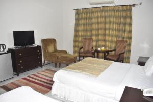 a hotel room with a bed and chairs and a tv at Pyramid International Guest House in Islamabad
