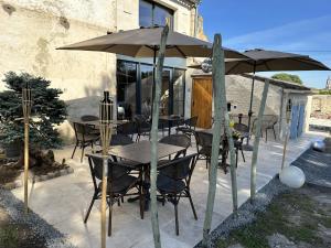 un patio con mesas, sillas y una sombrilla en Maison JEROBOAM en Saint-Estèphe
