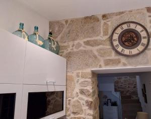 O berce casa rural camino Padrón Santiago في بادرون: ساعة على جدار حجري مع مزهريتين