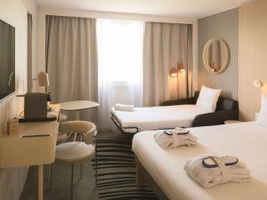 Habitación de hotel con 2 camas y escritorio en Novotel Bordeaux Lac en Burdeos