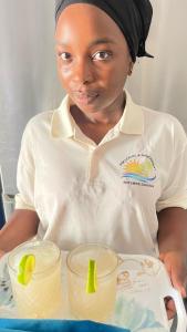 kobieta trzymająca tacę z dwoma kieliszkami lemoniady w obiekcie PM Lodge and Restaurant w mieście Matemwe