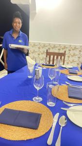 馬特姆維的住宿－PM Lodge and Restaurant，站在桌子旁的一位妇女,穿着蓝色桌布