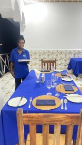 a woman standing in front of a table with a blue table cloth at PM Lodge and Restaurant in Matemwe