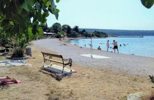 a bench on a beach with people in the water at Apartmani Ivan in Gornji Karin