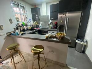 cocina con encimera con 2 taburetes y nevera en Habitacion privada en un dúplex, en Sevilla
