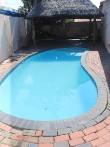 a large blue swimming pool with a thatch roof at Nomanini guest house Nelspruit in Nelspruit