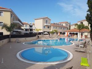 a swimming pool in a resort with chairs and buildings at Tranquil Kyklades BC6, WALK to BEACH in Paralimni