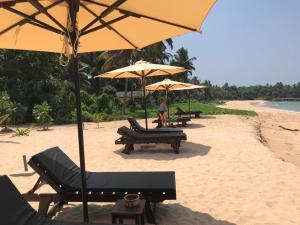 a beach with benches and umbrellas on the sand at THE Mangrove cave Hotel in Balapitiya