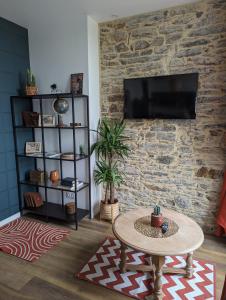 ein Wohnzimmer mit einem Tisch und einem TV an einer Steinmauer in der Unterkunft la Pléiade in Pont-Hébert