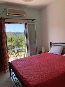 a bedroom with a bed with a red comforter and a balcony at Ammodares in Lixouri