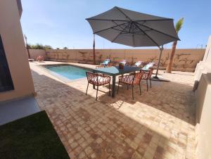 einen Tisch mit Stühlen und einen Sonnenschirm neben einem Pool in der Unterkunft Villa Saadia in Douar Bellouk