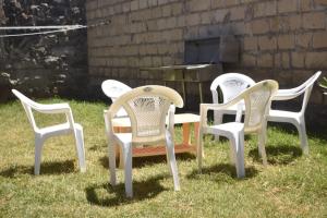 Mella homes limuru في Kiambu: أربعة كراسي بيضاء تجلس في العشب أمام شواية