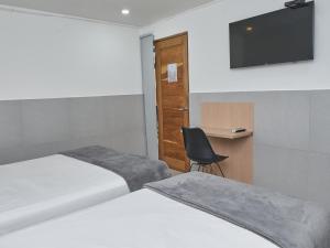 Habitación con 2 camas, silla y TV. en Stanza Hotel Medellin, en Medellín