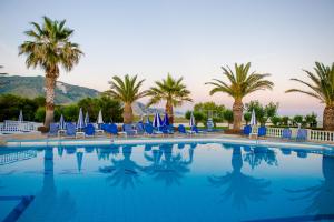 a large swimming pool with blue chairs and palm trees at Kalamaki Beach Hotel, Zakynthos Island in Kalamaki