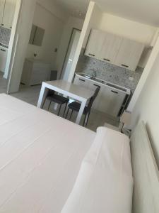 a white bedroom with a table and a kitchen at Ippocampo alba e tramonto in Ippocampo