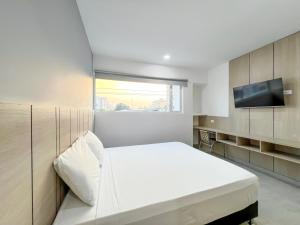 1 dormitorio con 1 cama blanca y TV de pantalla plana en Stanza Hotel Monteria, en Montería