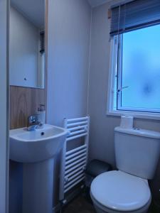 Charming 3-Bed Caravan in Colchester Mersea island في كولشستر: حمام به مرحاض أبيض ومغسلة
