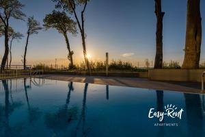 una piscina con puesta de sol detrás de los árboles en Double Blue Bien - Easy-Rent Apartments bezpośrednio przy plaży, en Rewal