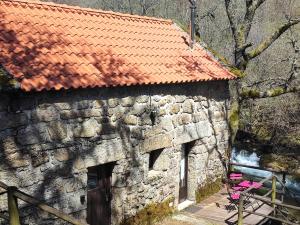 a stone building with a red roof and two pink chairs at Moinhos do Poço Verde - Nova Gestão in Castro Laboreiro