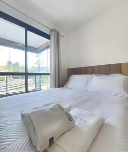 a bedroom with a white bed with a large window at Conforto no Caminho das árvores in Salvador