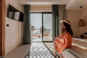 a woman sitting on a bed in a hotel room at Ostrako Beachside Suites in Agia Anna Naxos