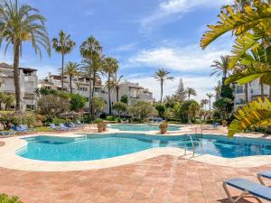 a large swimming pool with palm trees and buildings at Hanami Alcazaba Beach Duplex Sea View in Estepona